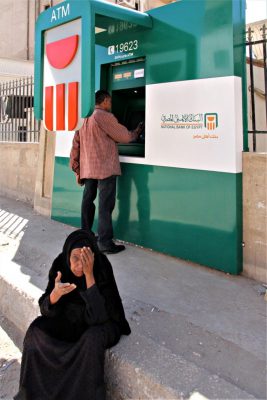 Bettlerin sitzt auf der Straße vor einem Bankautomaten