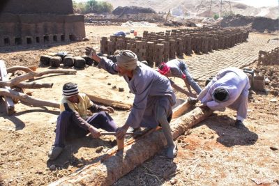 4 Männer spalten mit Axt, Keil und Muskelkraft einen Baumstamm