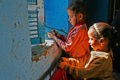 2 Kinder in roten Kleidern stehen an Fenster in blauer Wand