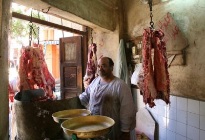 Fleischer in seinem Laden, große Fleischstücke haengen an der Decke