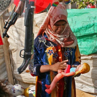 Frau betrachtet eine Puppe, daneben hängen (Spielzeug-)Gewehre