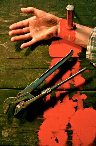 Arm mit Meisel an Holzplatte genagelt